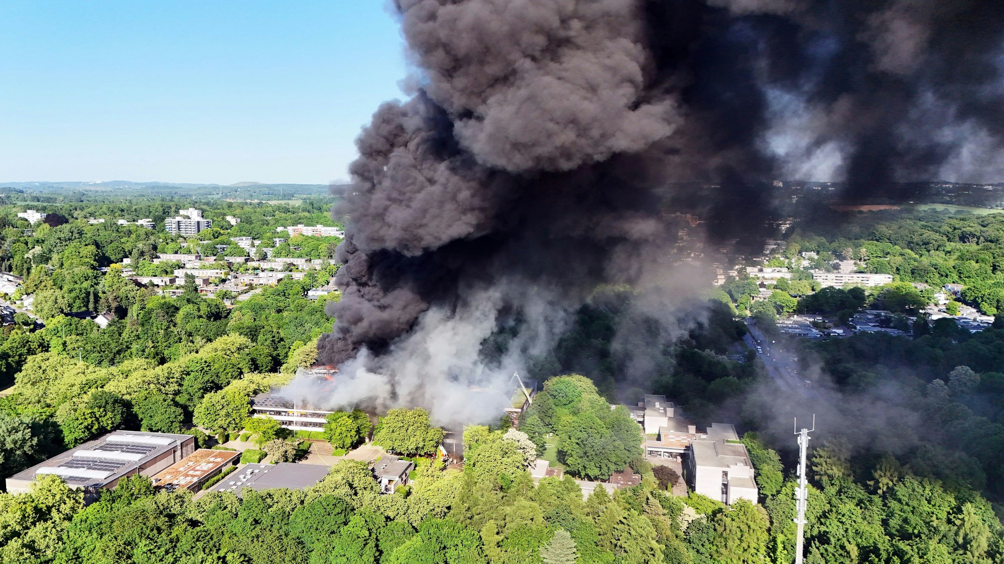 Eine schwarze Rauchwolke ist bei einem Großbrand über einem Gebäudekomplex mit mehreren Schulen im Kreis Mettmann zu sehen.
