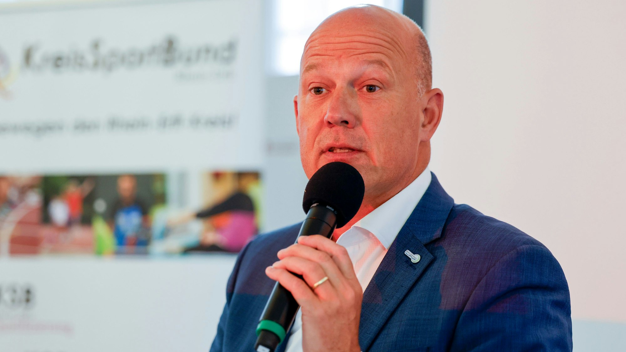 Auf dem Foto ist ein Mann mit Glatze zu sehen, der ein Mikro in der Hand hält.