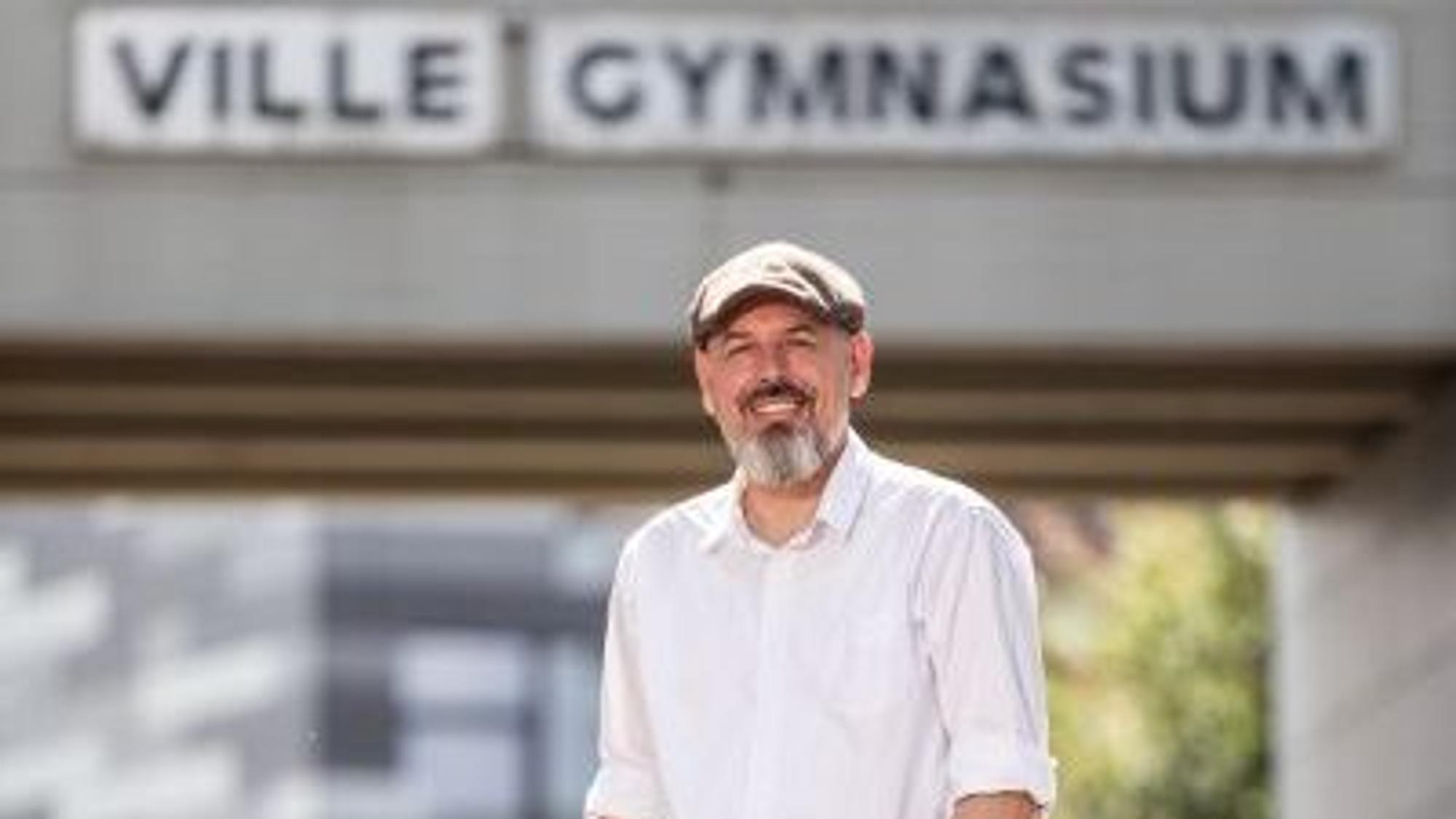 Auf dem Foto ist ein Mann mit Vollbart in weißem Hemd und einer Schiebermütze zu sehen.