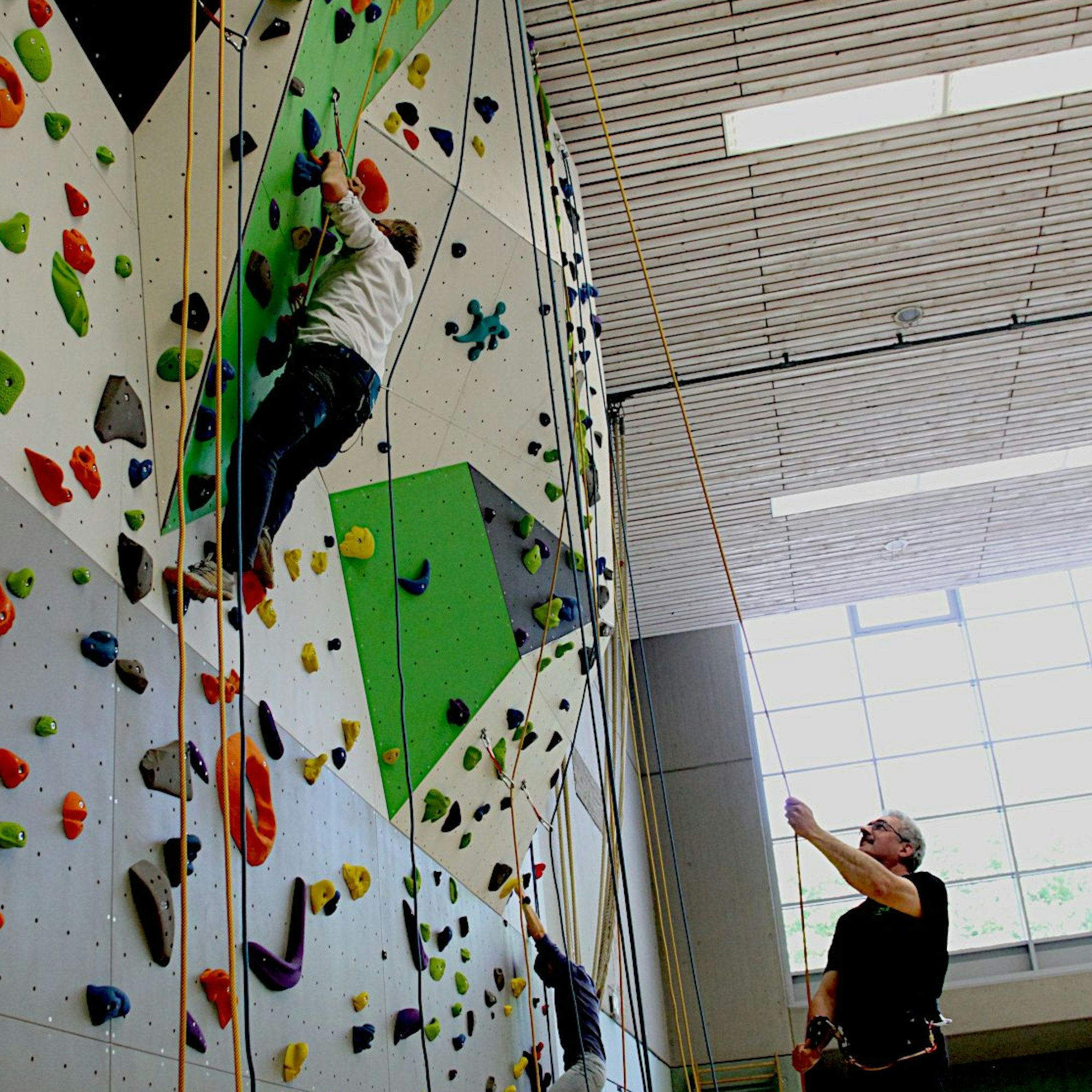 Henning Schneider klettert die Wand hoch, er wird von einem Mann gesichert.