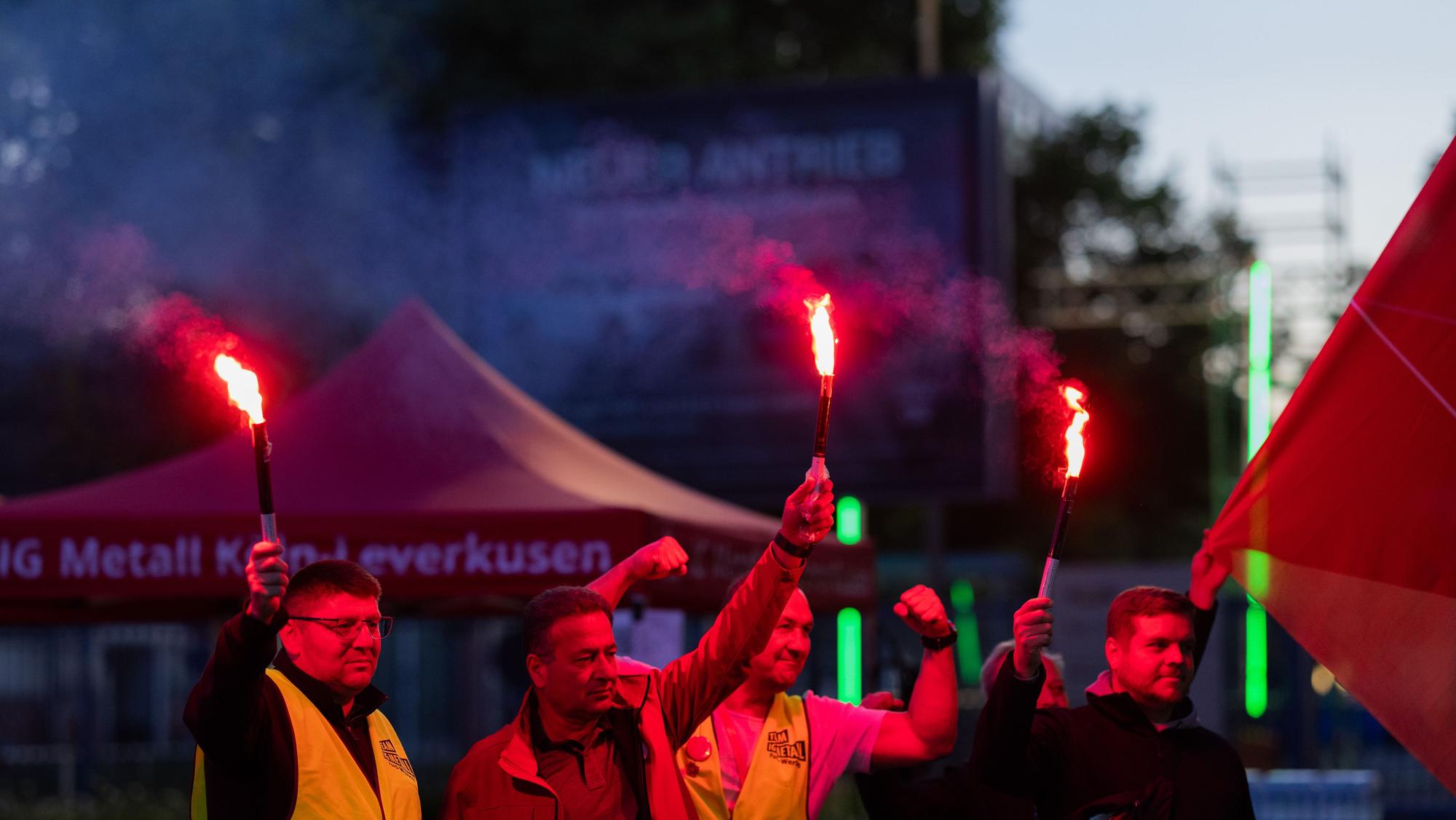 dpatopbilder - 14.05.2025, Nordrhein-Westfalen, Köln: Mitarbeiter mit brennenden Fackeln stehen beim ersten Streik vor den Kölner Ford-Werken. Bei den Kölner Ford-Werken kommt es erstmals zu einem Streik. Die Protestaktion gegen einen geplanten Stellenabbau an dem Standort mit 11.500 Beschäftigten soll am Mittwochmorgen beginnen und bis zum Ende der Nachtschicht am Donnerstagmorgen dauern, wie die IG Metall mitteilte. Foto: Rolf Vennenbernd/dpa +++ dpa-Bildfunk +++