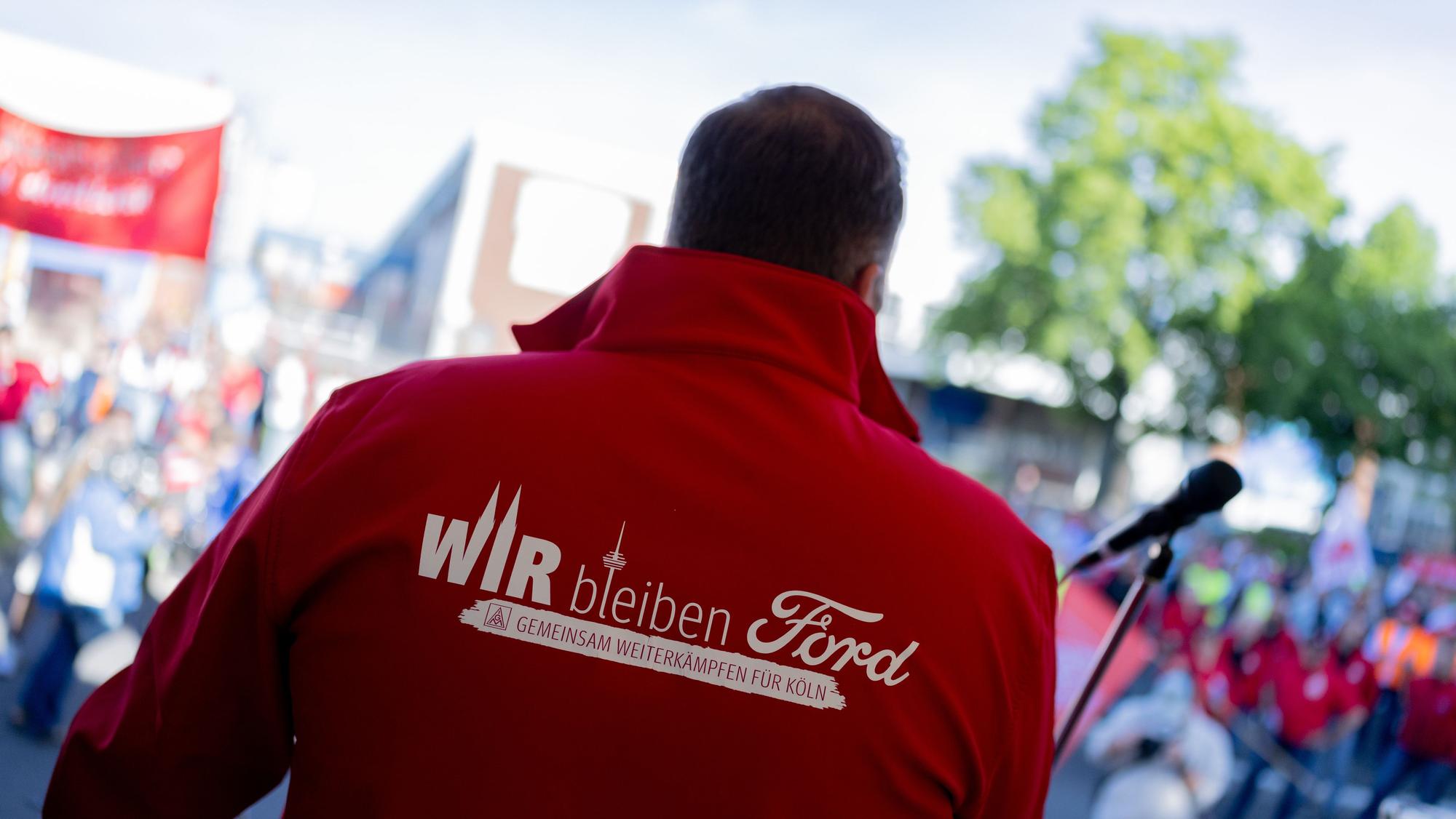14.05.2025, Nordrhein-Westfalen, Köln: Ein Mitarbeiter trägt eine Jacke mit der Aufschrift „Wir bleiben Ford - Gemeinsam weiterkämpfen für Köln“ beim ersten Streik der Geschichte vor den Kölner Ford-Werken. Bei den Kölner Ford-Werken kommt es erstmals zu einem Streik. Die Protestaktion gegen einen geplanten Stellenabbau an dem Standort mit 11.500 Beschäftigten soll am Mittwochmorgen beginnen und bis zum Ende der Nachtschicht am Donnerstagmorgen dauern, wie die IG Metall mitteilte. Foto: Rolf Vennenbernd/dpa +++ dpa-Bildfunk +++