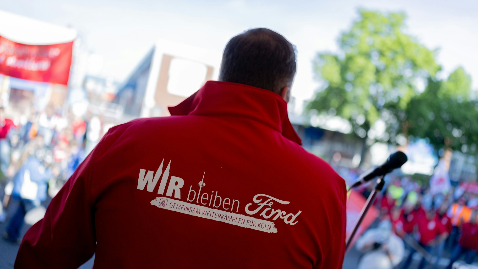14.05.2025, Nordrhein-Westfalen, Köln: Ein Mitarbeiter trägt eine Jacke mit der Aufschrift „Wir bleiben Ford - Gemeinsam weiterkämpfen für Köln“ beim ersten Streik der Geschichte vor den Kölner Ford-Werken. Bei den Kölner Ford-Werken kommt es erstmals zu einem Streik. Die Protestaktion gegen einen geplanten Stellenabbau an dem Standort mit 11.500 Beschäftigten soll am Mittwochmorgen beginnen und bis zum Ende der Nachtschicht am Donnerstagmorgen dauern, wie die IG Metall mitteilte. Foto: Rolf Vennenbernd/dpa +++ dpa-Bildfunk +++