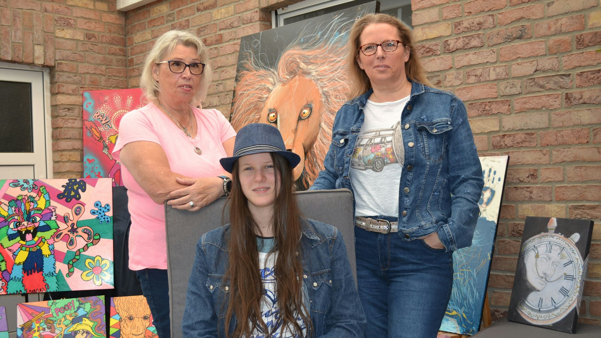 Großmutter und Mutter stehen und die Tochter sitzt vor den Bildern, die sie gemalt haben.