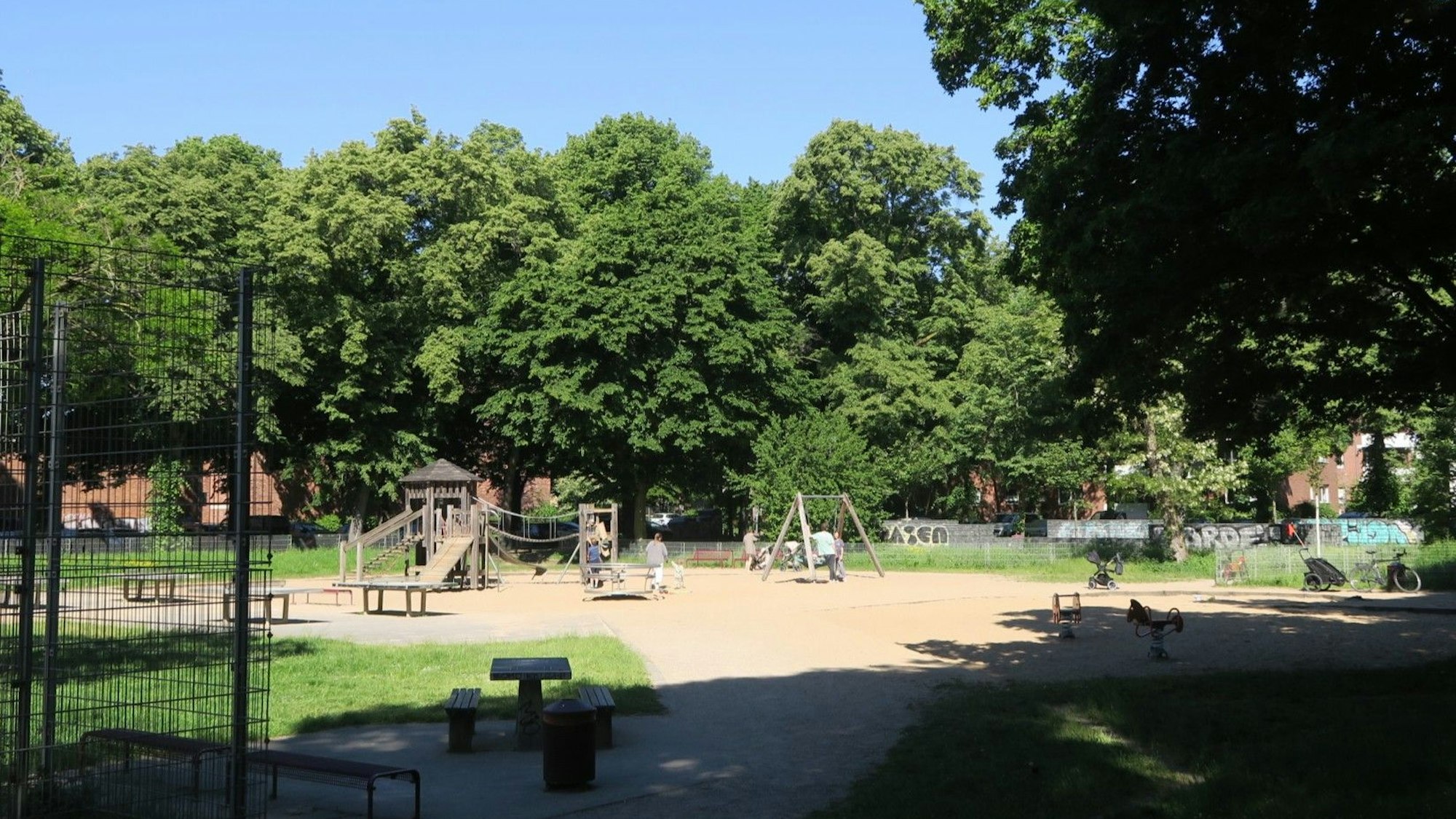 Ein von Bäumen umgebener Spielplatz mit Tischtennisplatten.