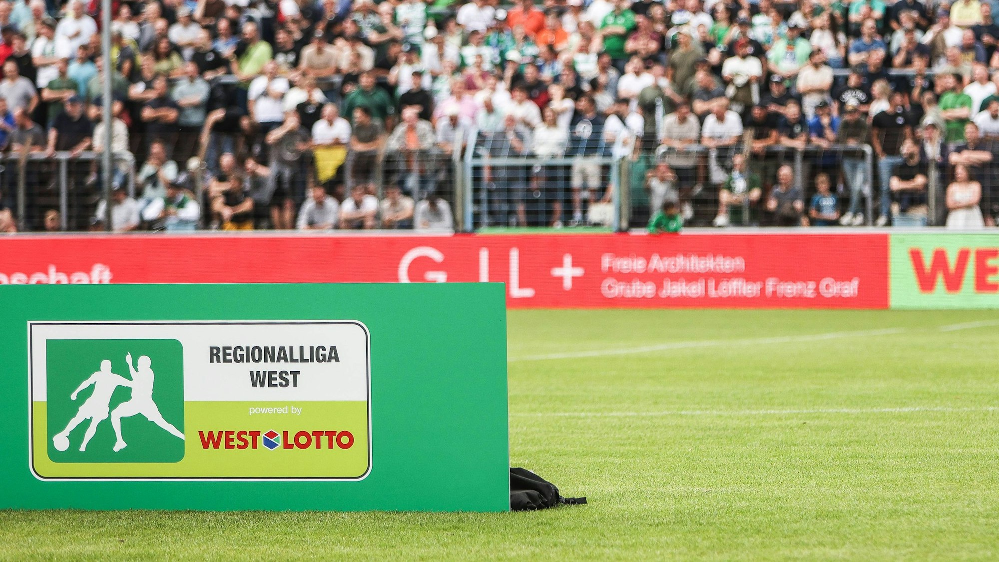Vor einer Fankurve in einem Fußballstadion steht ein Schild mit der Aufschrift „Regionalliga West“.
