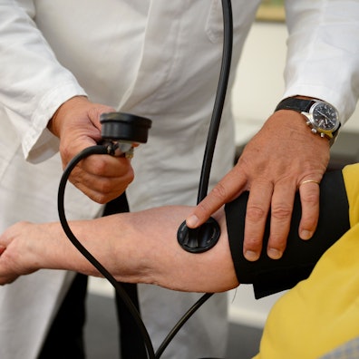 Ein Hausarzt misst in seiner Praxis einer Patientin den Blutdruck.