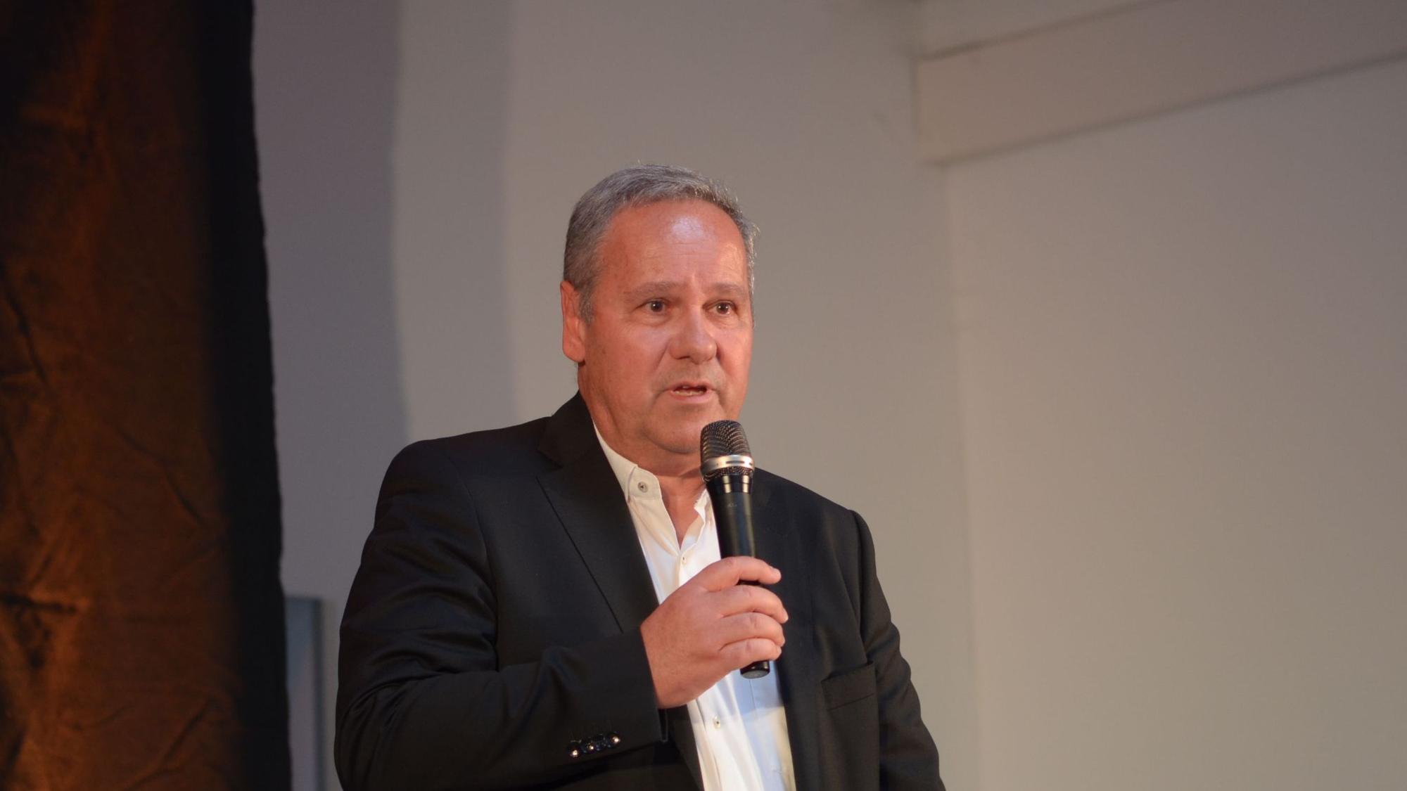 Das Bild zeigt einen Mann, der in ein Mikrofon spricht.