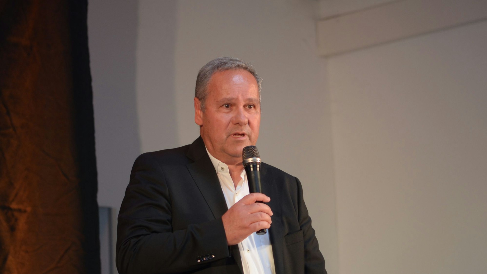 Das Bild zeigt einen Mann, der in ein Mikrofon spricht.