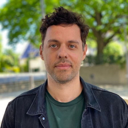 Ein Porträt von Stephan Hellweg. Im Hintergrund ist verschwommen die Herz-Jesu-Kirche zu sehen.