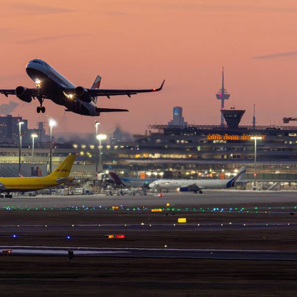 Flugverkehr vor der Skyline von Köln und den Terminals bei Sonnenuntergang und klarem Himmel am Flughafen Köln/Bonn