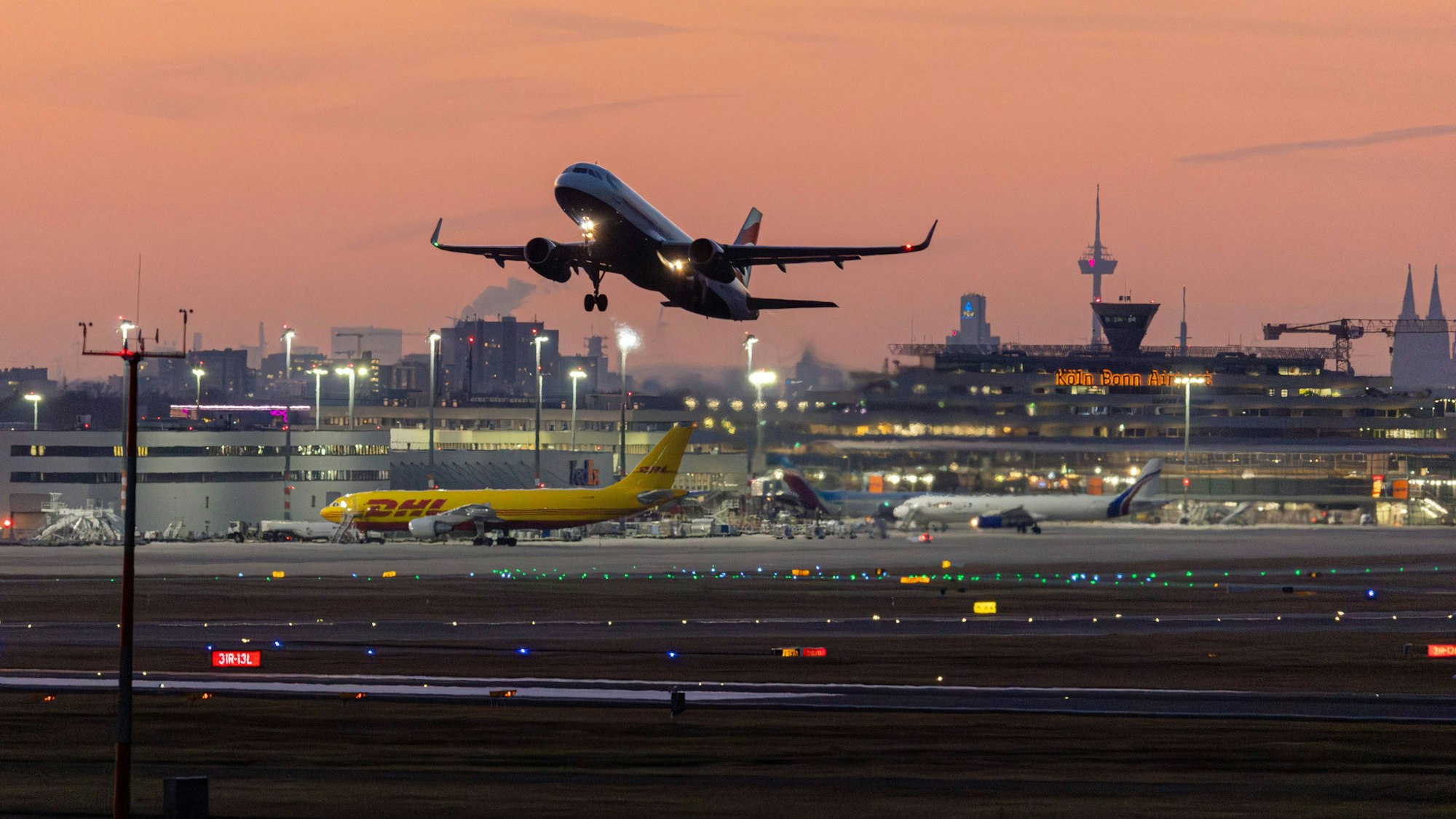 Flugverkehr vor der Skyline von Köln und den Terminals bei Sonnenuntergang und klarem Himmel am Flughafen Köln/Bonn