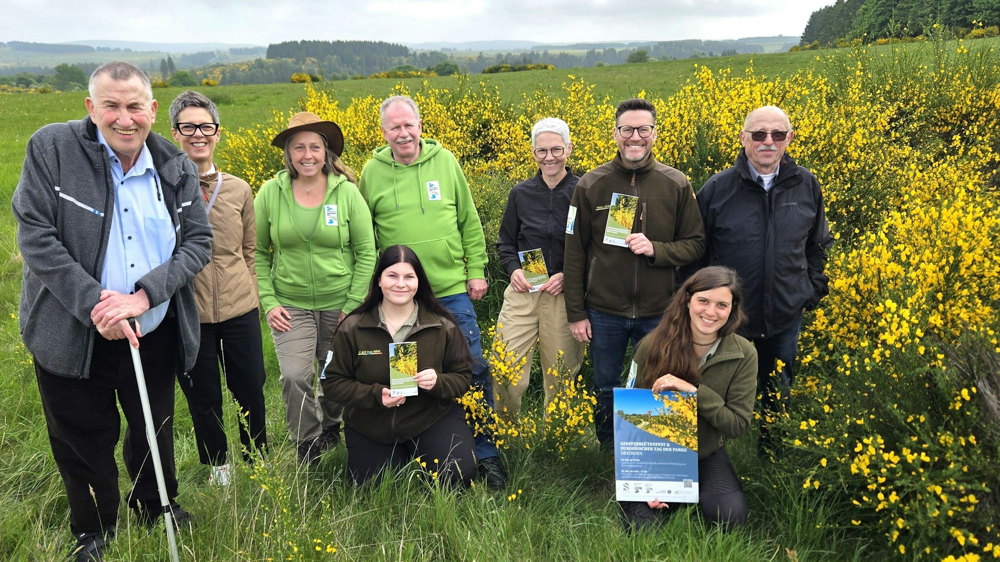 Vertreterinnen und Vertreter der beteiligten Organisationen haben sich neben blühenden Ginsterbüschen zum Gruppenbild aufgestellt.