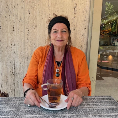 Zu sehen ist Heide Hansen-Fischer an einem Tisch vor einem Getränk sitzend.