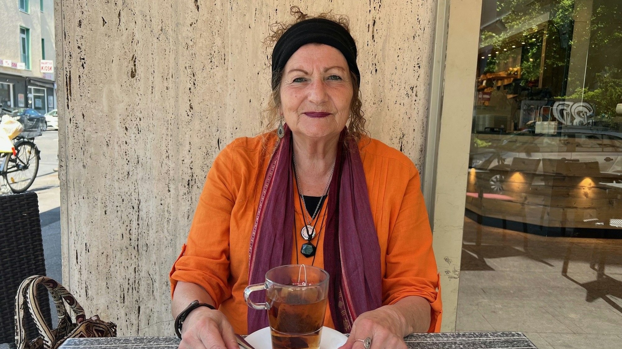 Zu sehen ist Heide Hansen-Fischer an einem Tisch vor einem Getränk sitzend.