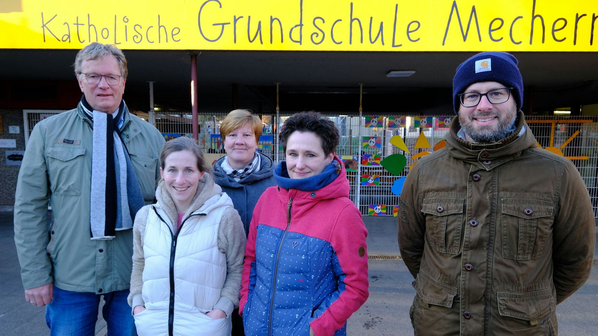 Die drei Frauen und zwei Männer stehen unter einem Schild mit der Aufschrift „Katholische Grundschule Mechernich“.