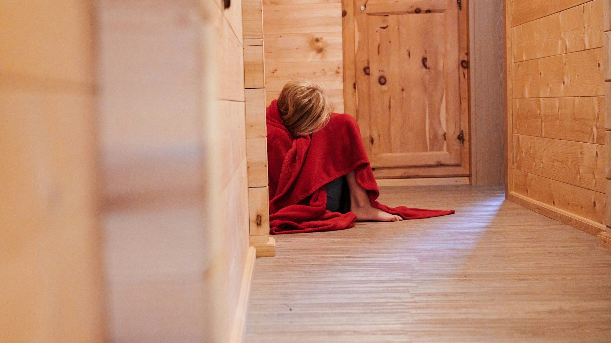 Ein Kind ist in eine Decke gewickelt und kauert auf dem Boden eines Hausflures (gestellte Szene).