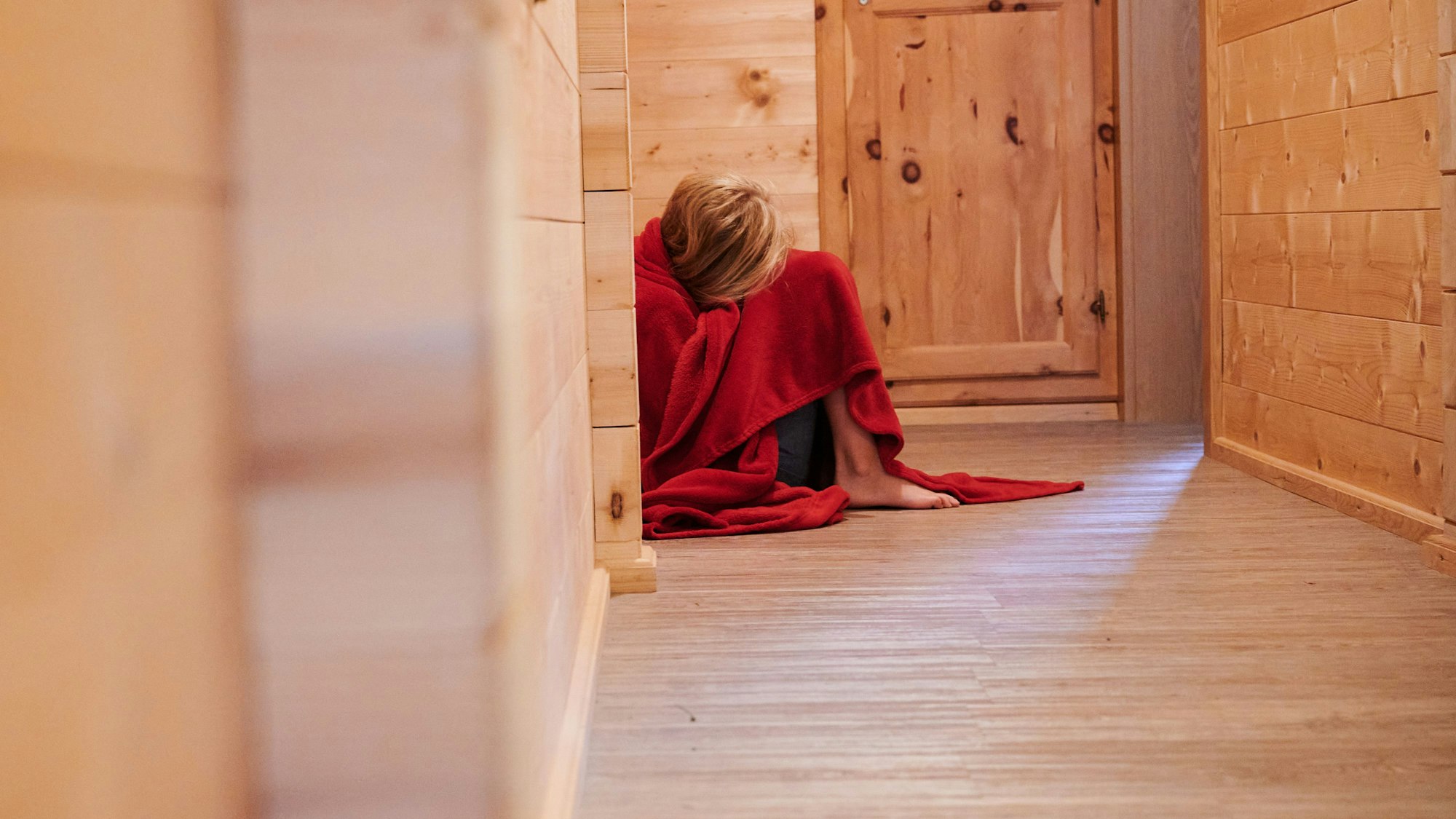 ARCHIV - 01.08.2022, Österreich, Mayrhofen: ILLUSTRATION - Ein Kind ist in eine Decke gewickelt und kauert auf dem Boden eines Hausflures (gestellte Szene). (zu dpa: «Fast jede fünfte Frau weltweit hat als Kind sexuelle Gewalt erlebt») Foto: Annette Riedl/dpa +++ dpa-Bildfunk +++