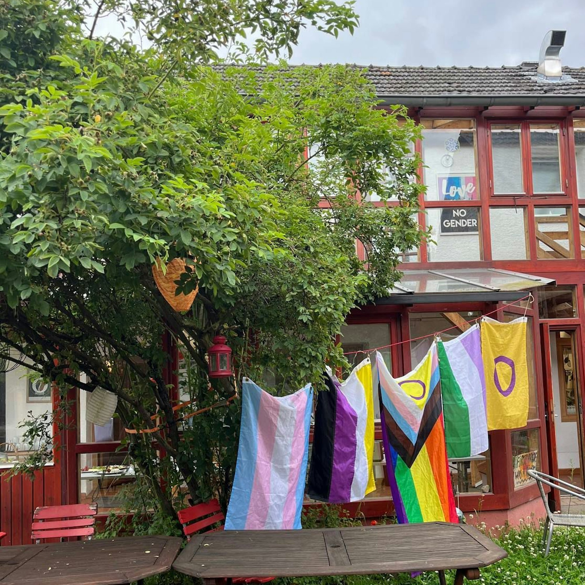 Eine Fachwerkhausfassade, davor steht ein Baum. Zwischen Baum und Vordach sind verschiedene Pride-Flaggen aufgehängt worden.