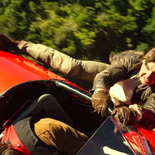 Tom Cruise hängt als Ethan Hunt an einem fliegenden, roten Doppeldecker-Flugzeug.