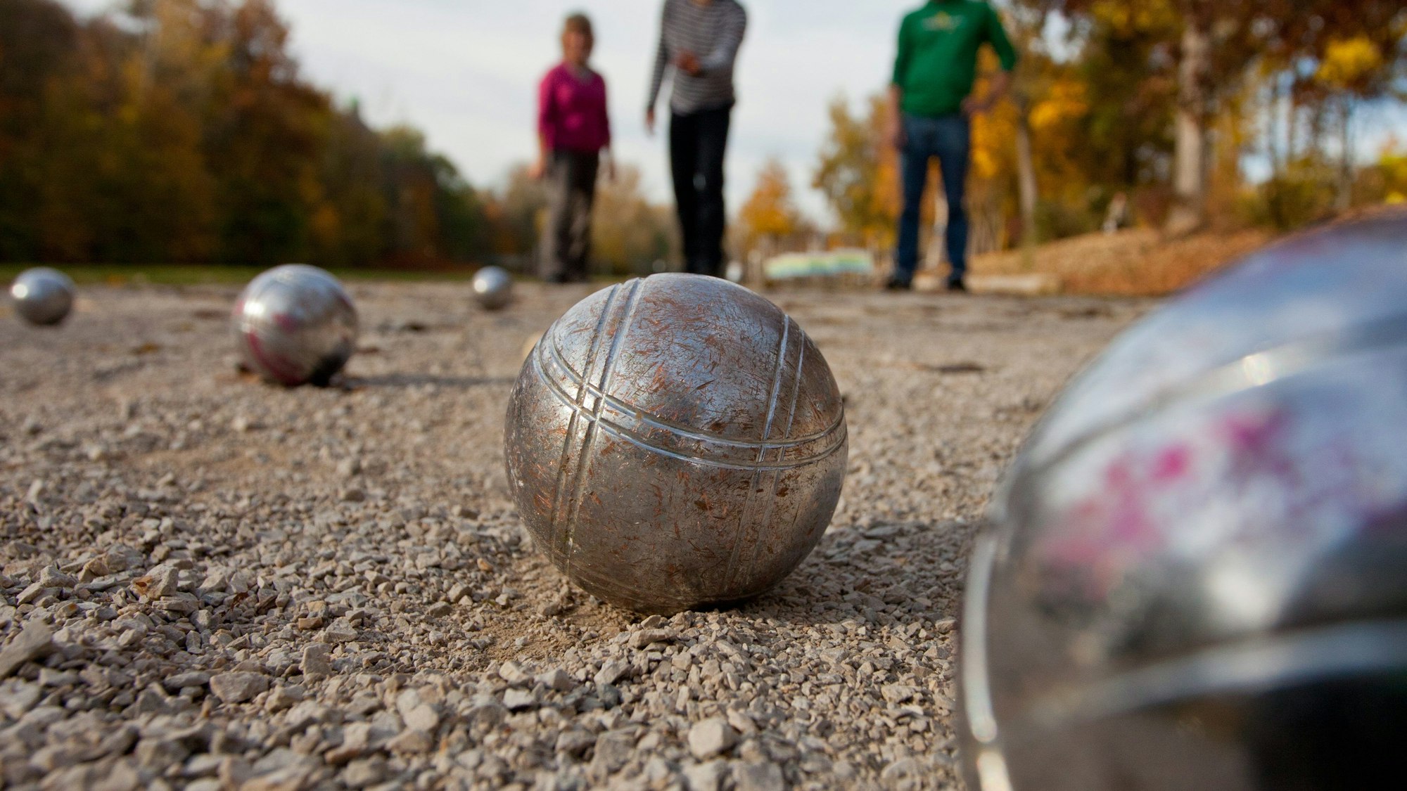 Zwei Männer und eine Frau spielen Boule.