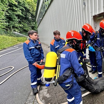 Junge Feuerwehrleute in Atemschutz und Sicherheitshelm tragen einen Dummy aus der Gefahrenzone.