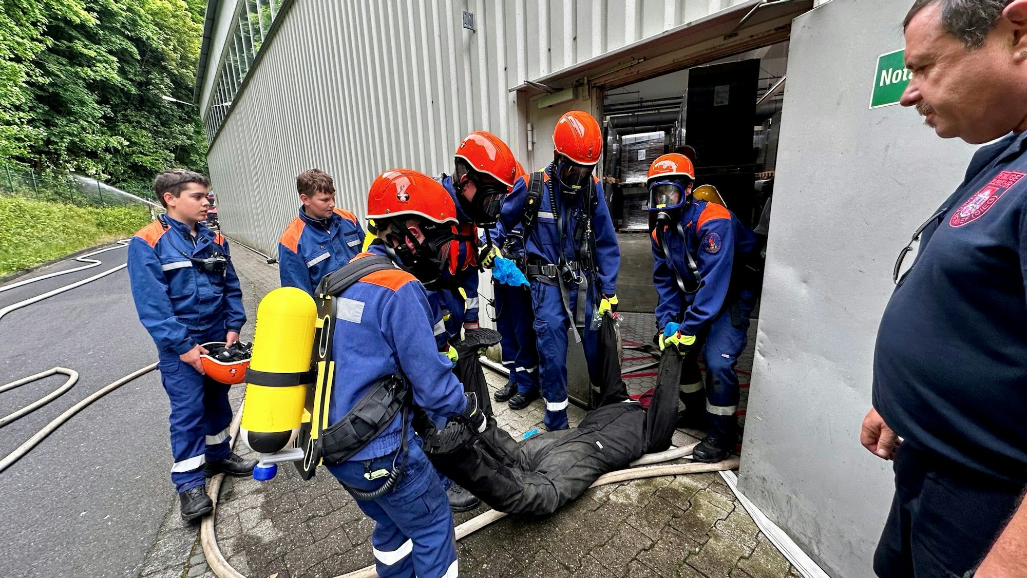 Junge Feuerwehrleute in Atemschutz und Sicherheitshelm tragen einen Dummy aus der Gefahrenzone.