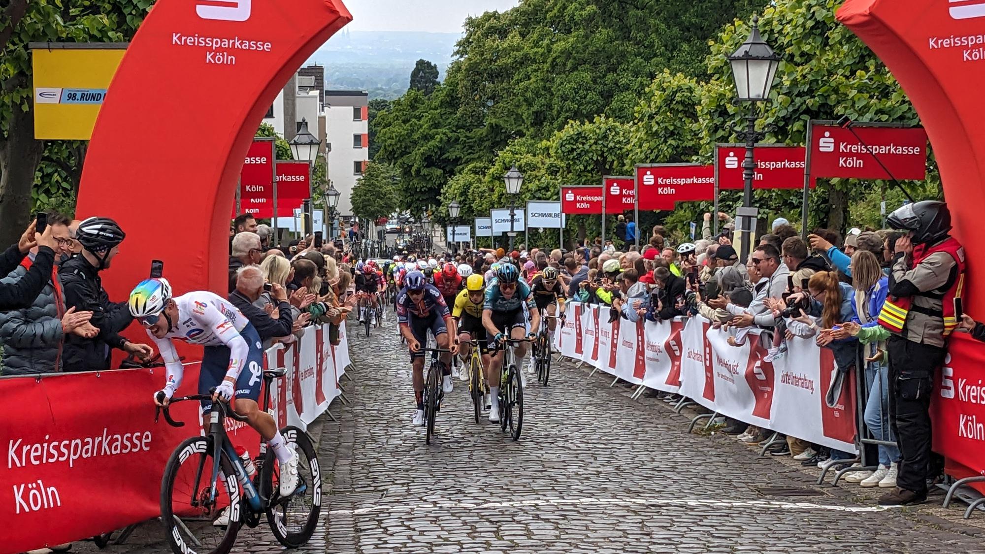 Zu sehen ist eine Gruppe Radfahrer, die ins Ziel auf einem Anstieg einrollen.