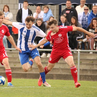 Das Bild zeigt einen Fußballer, dem zwei Gegner den Ball abnehmen wollen.