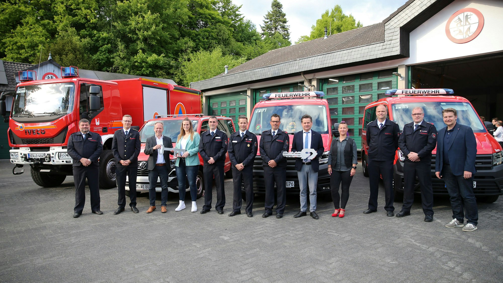 Eine Gruppe steht vor vier Feuerwehrfahrzeugen.