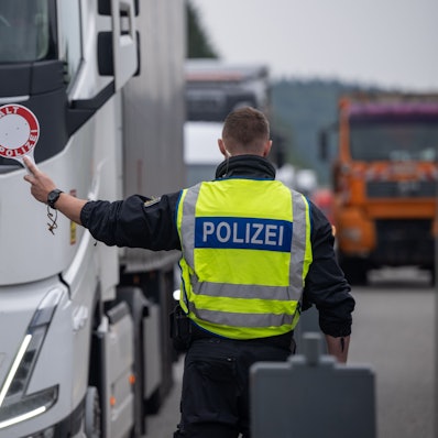 Polizisten kontrollieren Fahrzeuge zu Beginn der Grenzkontrollen an allen deutschen Landesgrenzen. Ein Polizist in Warnweste hält eine Kelle auf der „Halt Polizei“ steht, in Richtung eines LKW. (Archivbild)