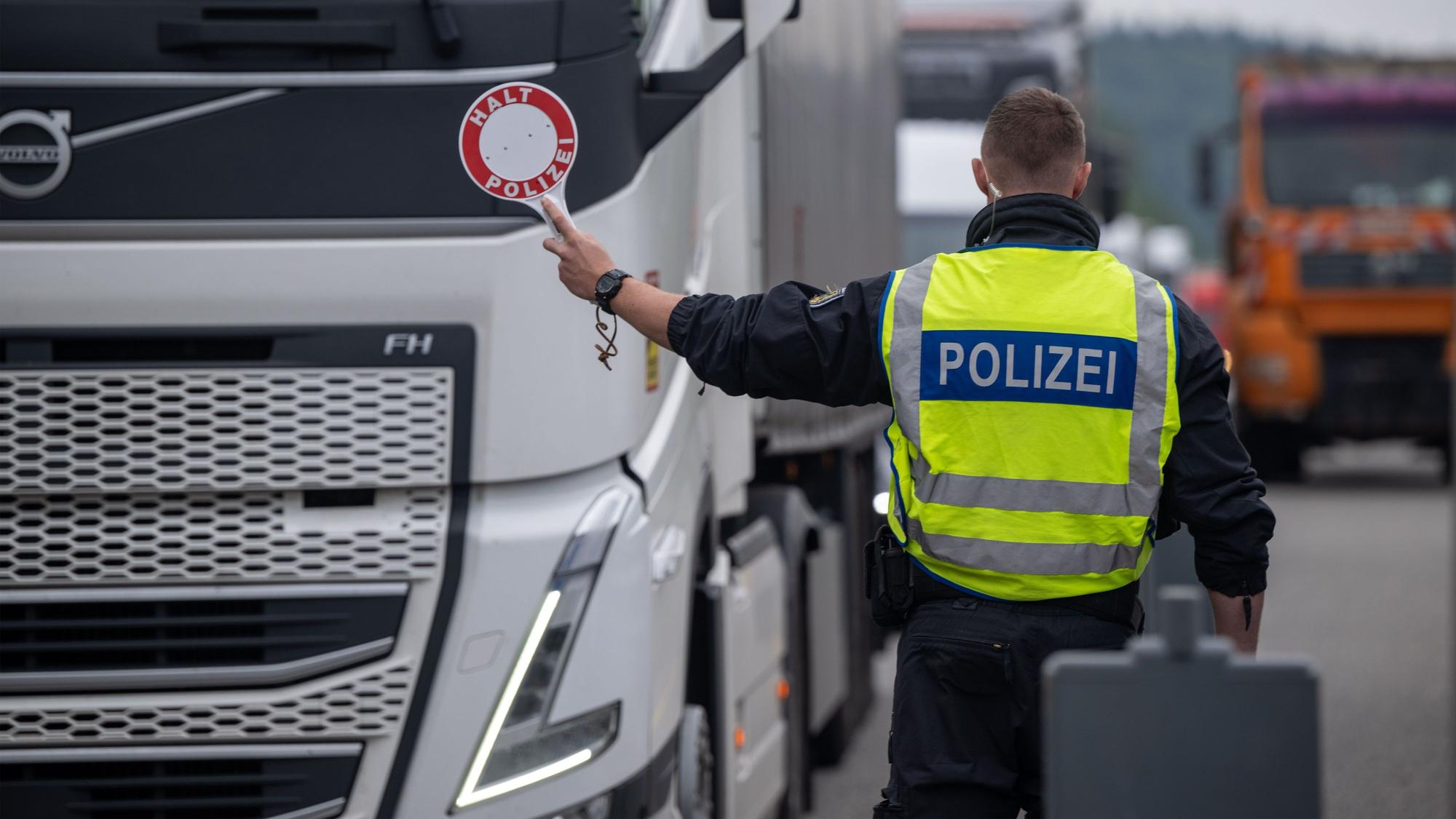 Polizisten kontrollieren Fahrzeuge zu Beginn der Grenzkontrollen an allen deutschen Landesgrenzen. Ein Polizist in Warnweste hält eine Kelle auf der „Halt Polizei“ steht, in Richtung eines LKW. (Archivbild)