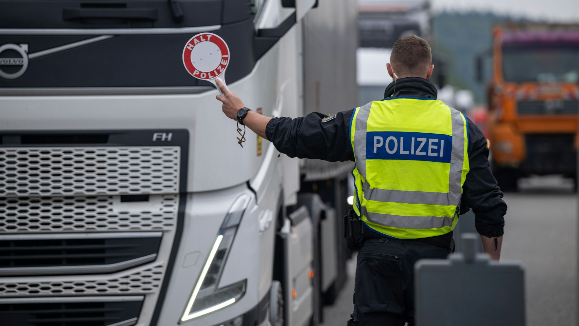 Polizisten kontrollieren Fahrzeuge zu Beginn der Grenzkontrollen an allen deutschen Landesgrenzen. Ein Polizist in Warnweste hält eine Kelle auf der „Halt Polizei“ steht, in Richtung eines LKW. (Archivbild)