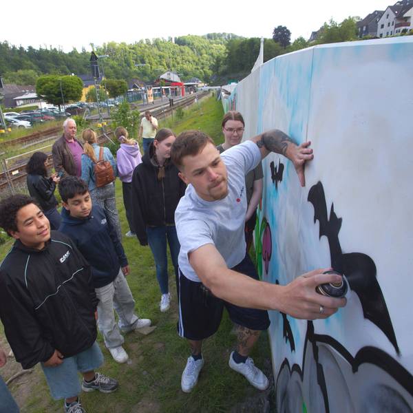 Das Foto zeigt einen Sprayer an einer Mauer und jugendliche Zuschauer.