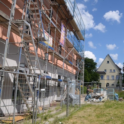 Ein eingerüstetes Gebäude, eine Rasenfläche und ein Kirchturm.