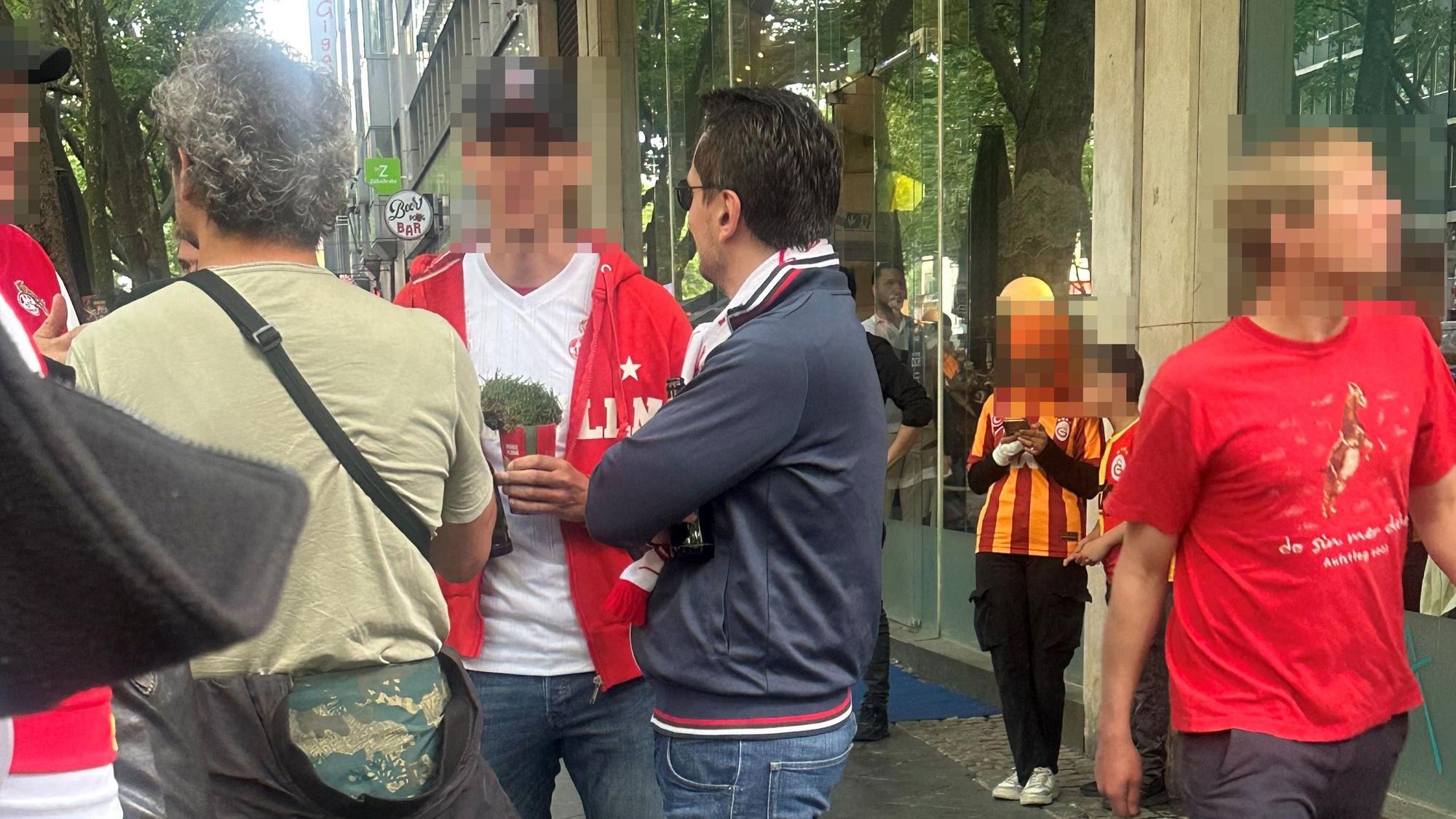Ein FC-Fan trägt ein Rasenstück, mutmaßlich aus dem Rhein-Energie-Stadion, in einem Getränkebecher mit sich herum.