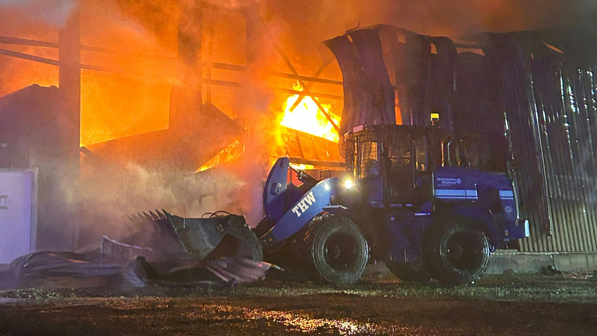 Mit einem Radlader zieht ein THW-Helfer in der Nacht beim Brand in Ollheim Teile der Hallenwand beiseite.