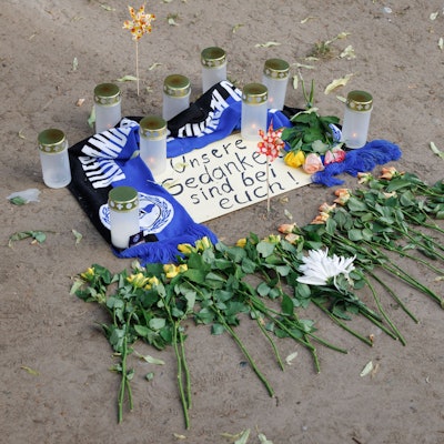 Bielefeld: Kerzen und ein Fanschal von Arminia Bielefeld sind an einem Tatort in der Innenstadt zu sehen. Nach dem Angriff eines Mannes auf mindestens fünf Menschen vor einer Bar in Bielefeld ist ein Tatverdächtiger festgenommen worden.