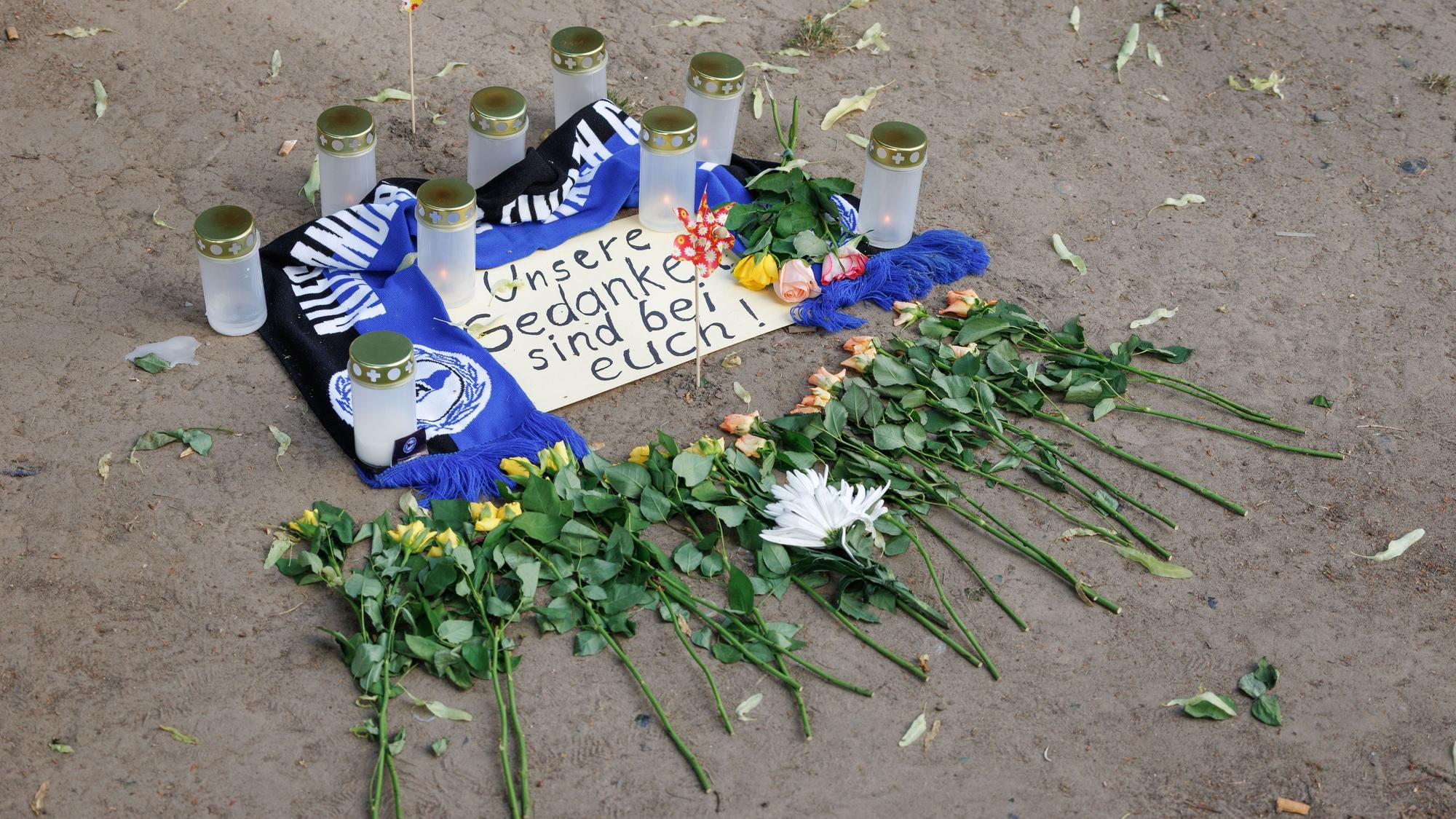 Bielefeld: Kerzen und ein Fanschal von Arminia Bielefeld sind an einem Tatort in der Innenstadt zu sehen. Nach dem Angriff eines Mannes auf mindestens fünf Menschen vor einer Bar in Bielefeld ist ein Tatverdächtiger festgenommen worden.
