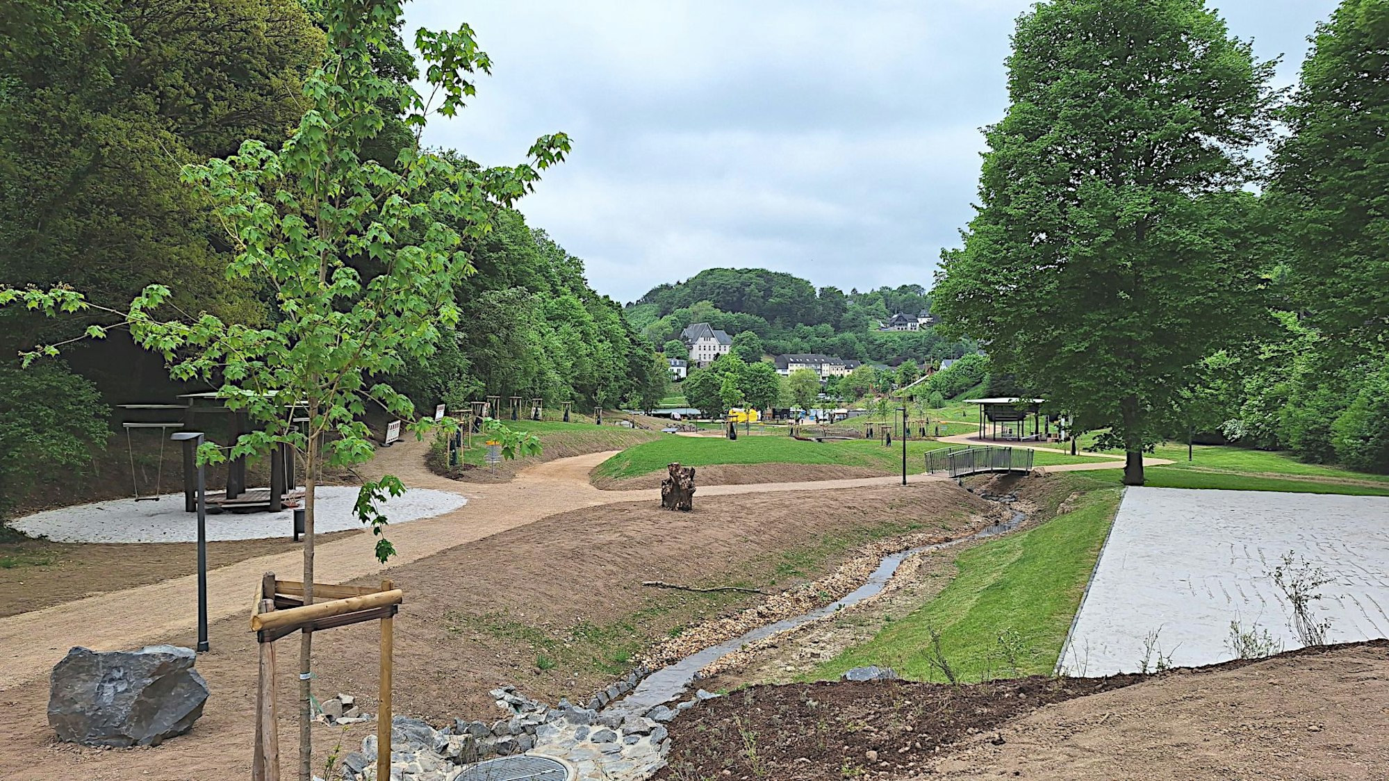Das Bild zeigt die neue Parkanlage in Blankenheim mit Sandwegen und einem Bach.
