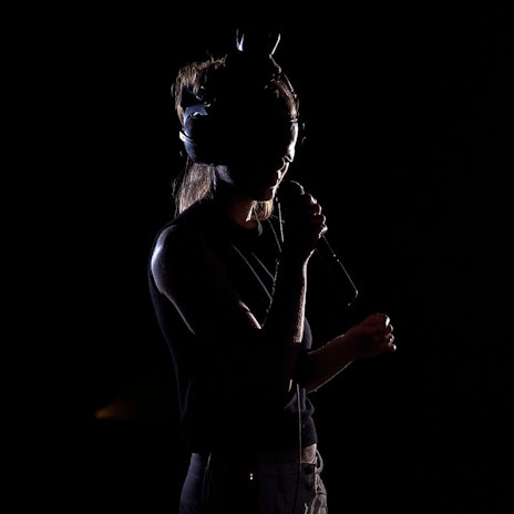 Eine junge Frau trägt im Dunkeln eine VR-Brille und spricht in ein Mikrofon.