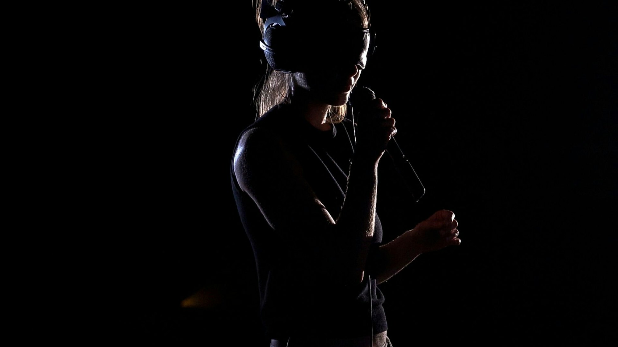 Eine junge Frau trägt im Dunkeln eine VR-Brille und spricht in ein Mikrofon.