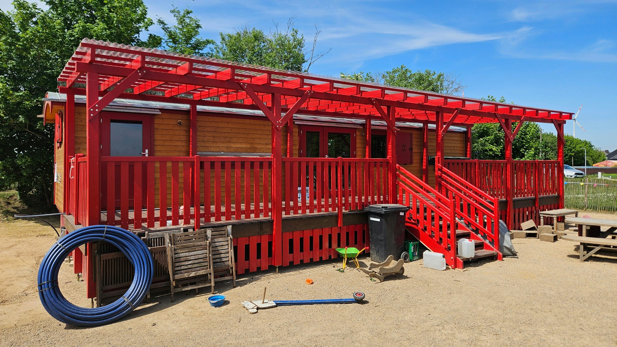 Vor einem Bauwagen steht eine rot angestrichene Holz-Veranda.
