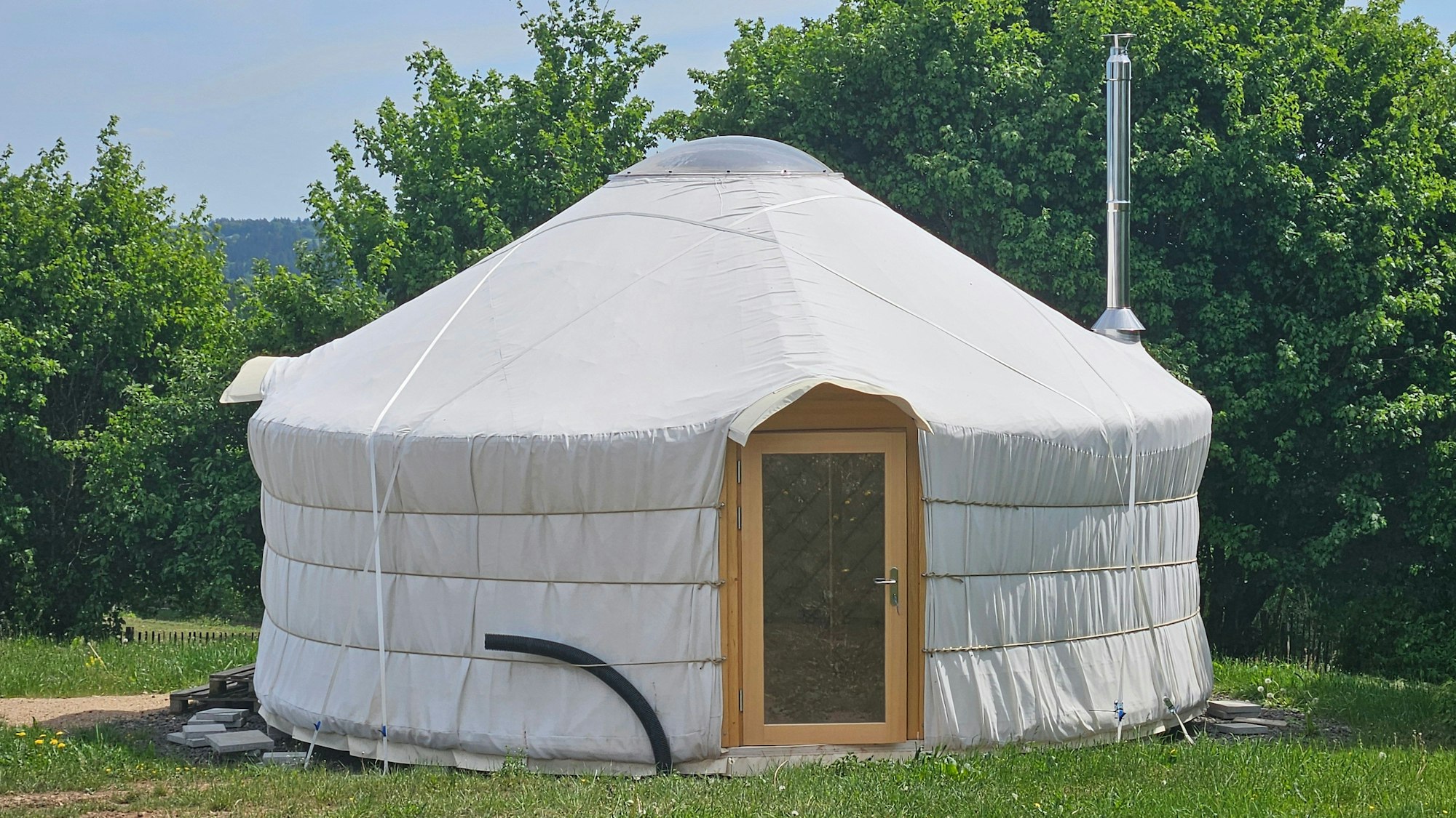Eine weiße Jurte mit einer hölzernen Tür auf dem Gelände des Waldkindergartens Ettelscheid.