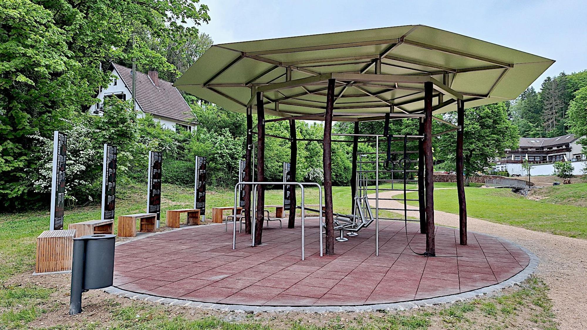 Fitnessgeräte stehen unter einem Pavillon in einem Park.