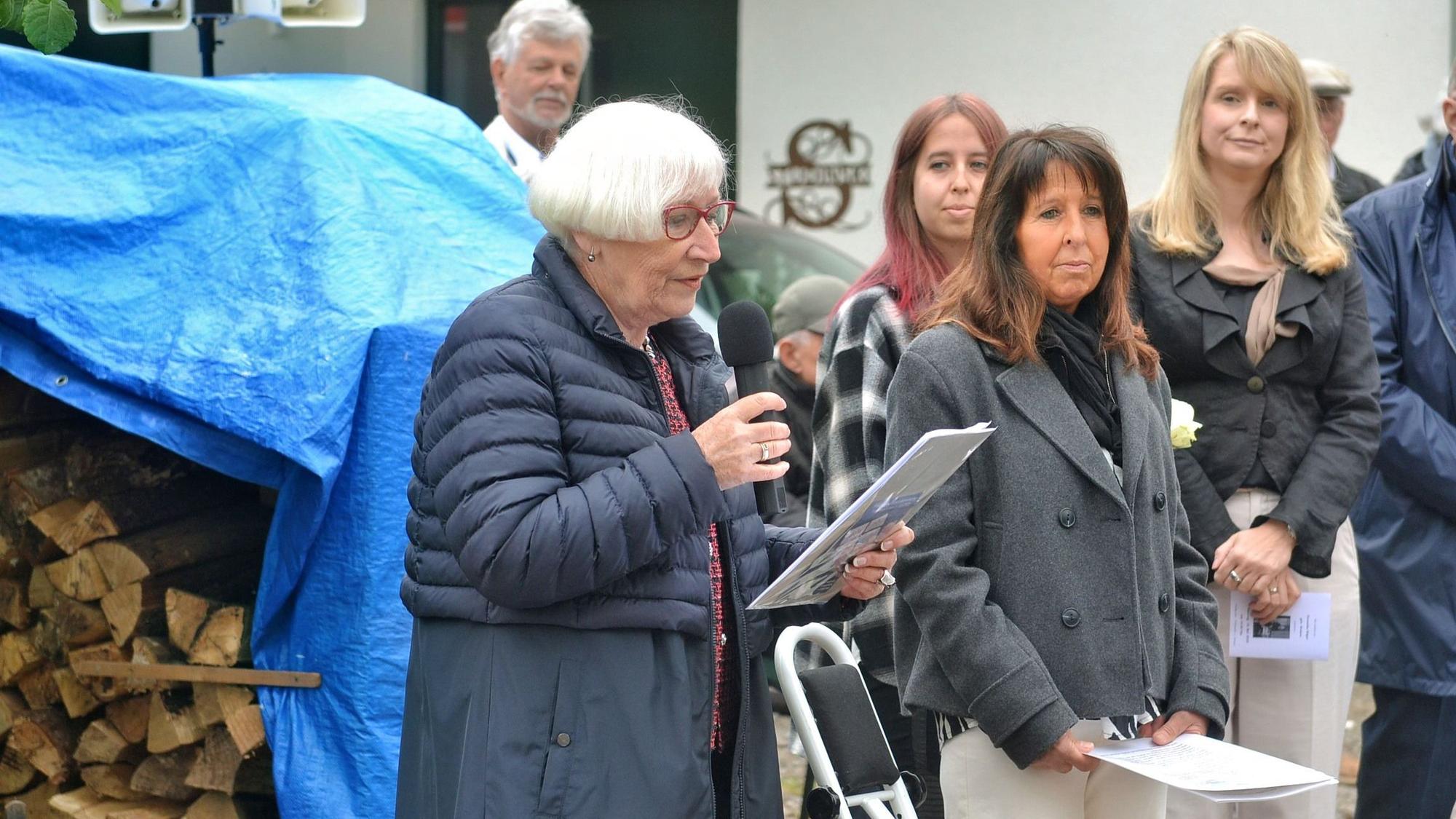 Gisela Freier hält ein Mikrofon und ein Manuskript in den Händen. Daneben stehen einige der Besucher.