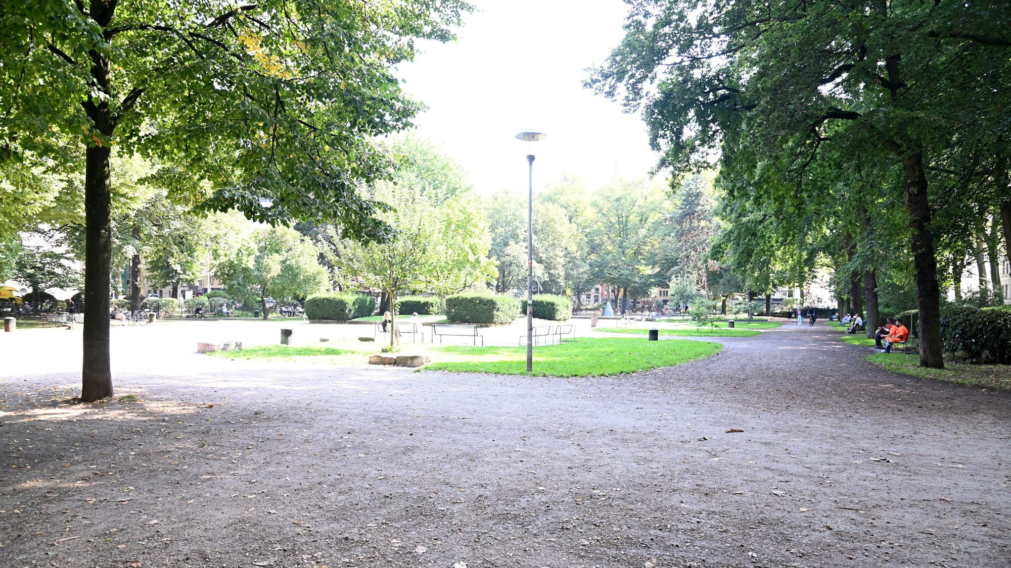 Schotterwege und Grünflächen mit hohen Bäumen am Rand sind zu sehen.