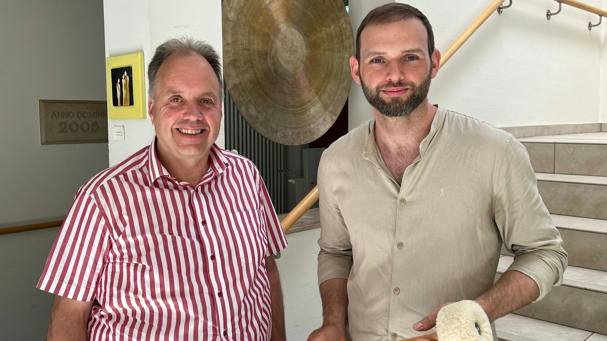 Zwei Männer stehen in einem Hausflur vor einer Gongschale.