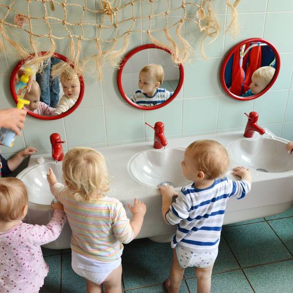 In einer Kita waschen sich die ein-bis zweijährigen Mädchen und Jungen mit ihrer Erzieherin die Hände.