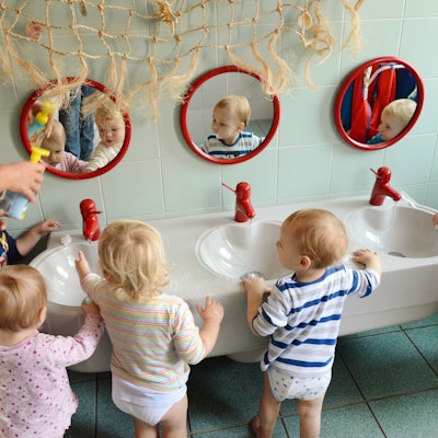 In einer Kita waschen sich die ein-bis zweijährigen Mädchen und Jungen mit ihrer Erzieherin die Hände.